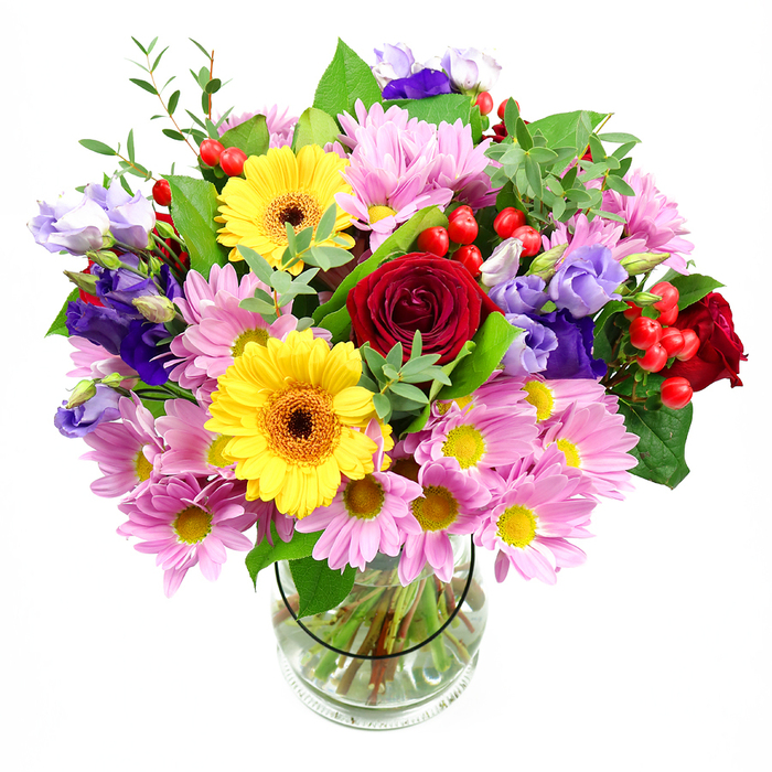An abundant, garden-style bouquet rises from a clear glass vase, set before a white background that throws every detail into sharp relief. At its centre, sumptuous deep red roses bloom with velvety petals arranged in rich spirals, giving the design a romantic and slightly dramatic focus. Nearby, two radiant yellow gerbera daisies with deep brown-orange centres stand proudly, their broad, daisy-shaped petals spreading outward like warm little suns, bringing a sense of optimism that feels right at home in Farnborough's friendly residential streets. Wrapping around these statement flowers is a generous layer of pastel pink and lilac daisies or chrysanthemums, each bloom defined by many slim petals encircling tiny yellow hearts. These softer flowers lend a feathery texture and gentle colour that balance the bolder tones. Winding through the daisies, elegant stems of purple and lavender lisianthus rise and curve, their bell-shaped blossoms and slightly ruffled edges introducing a refined, cool note, reminiscent of the calm you find in the green spaces around Southwood Woodland. Punctuating the design, glossy red hypericum berries cluster in small groups, their smooth, rounded shapes providing a playful contrast against the petals. A tapestry of foliage in varied greens frames and supports the blooms, from wide, dark leaves that anchor the composition to lighter, airy sprigs that add height and movement, suggesting a bouquet freshly gathered from a local garden. The transparent vase reveals the carefully trimmed stems and clear water inside, testifying to the freshness and skill behind the arrangement. This vibrant composition feels ideal for celebrating special occasions, offering congratulations, or bringing a colourful burst of joy to homes, workplaces, and celebrations across Farnborough.